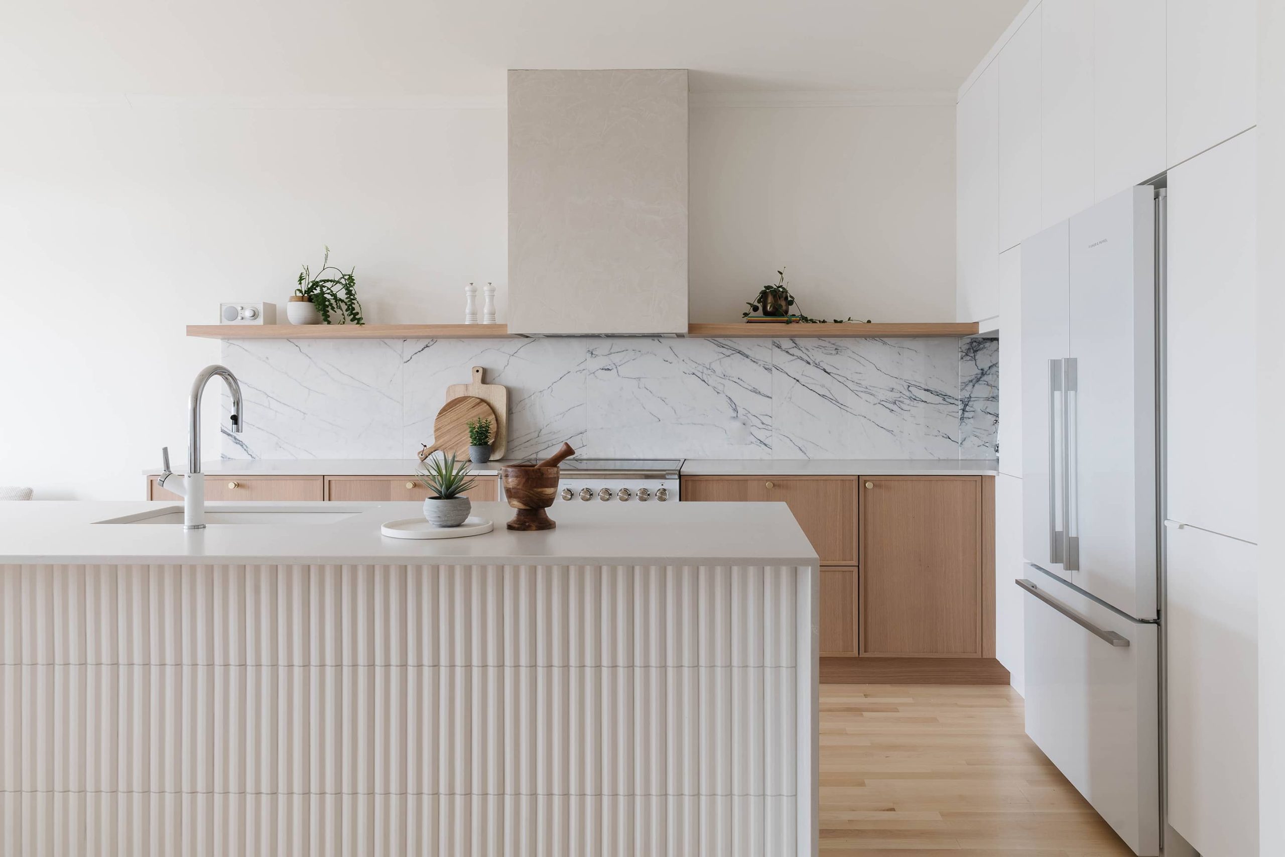 Cuisine sur mesure avec armoires en bois clair et îlot central cannelé, projet Groupe Cartier