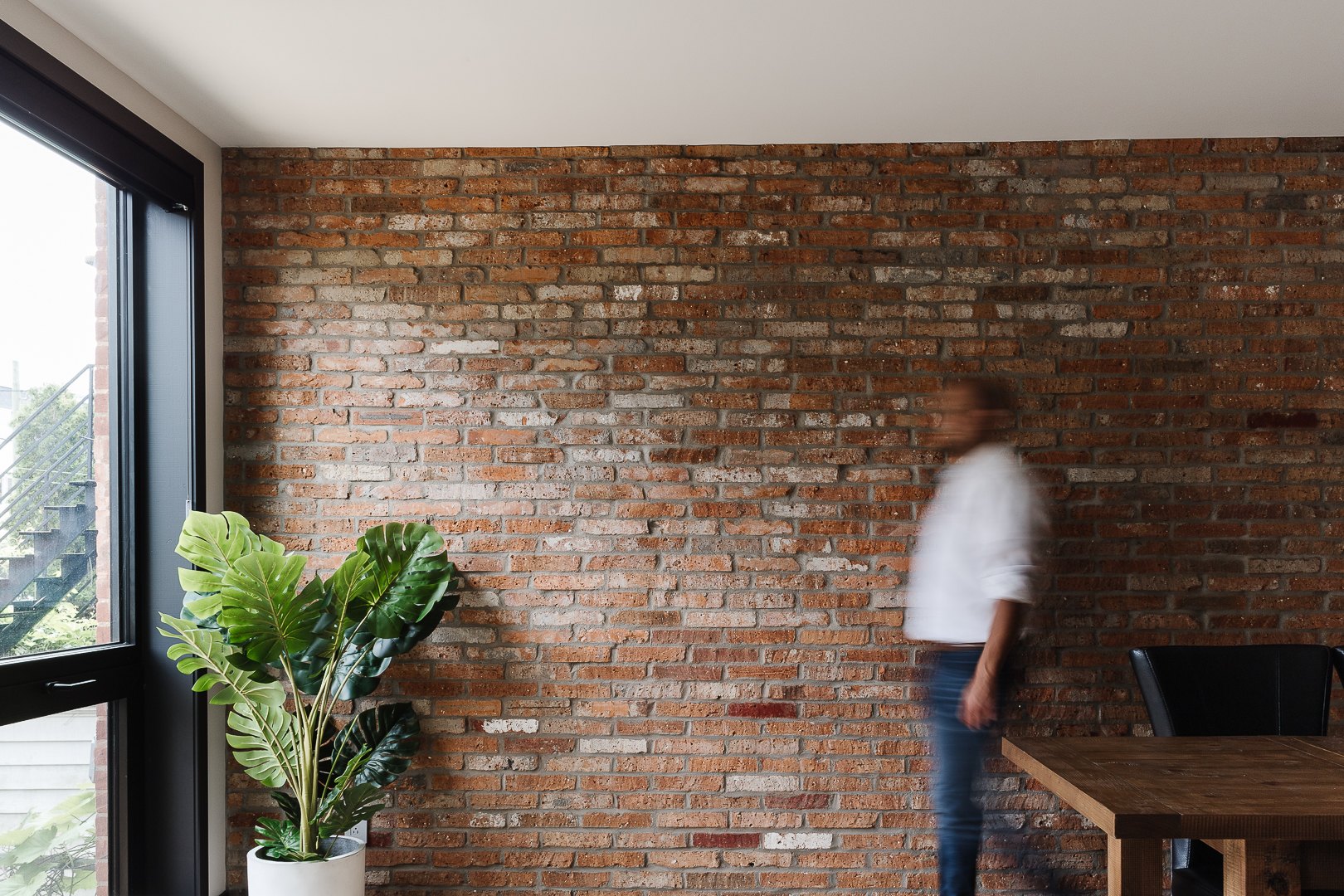 Mur de briques apparentes et grandes fenêtres noires dans la salle à manger, Résidence Lanaudière, Montréal